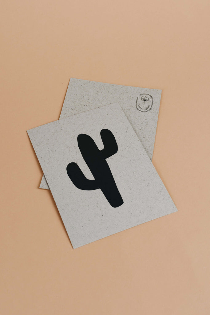 Postcard with light grey grass paper material and black cactus illustration on it.