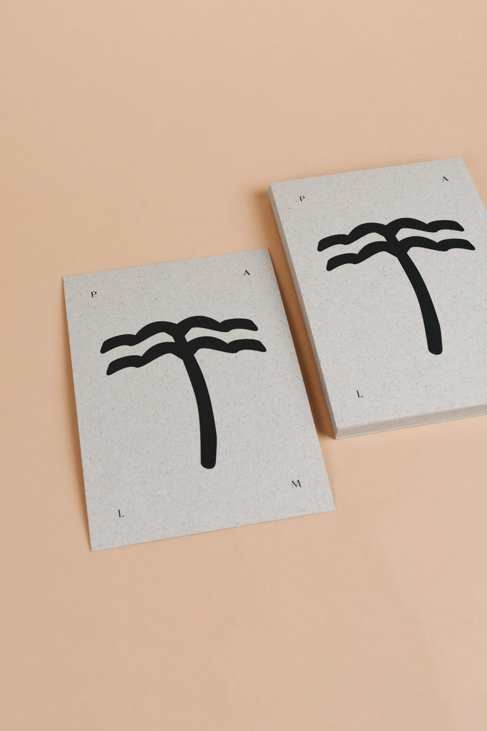Palm tree postcard with black and light grey grass paper material and minimalistic palm tree illustration on it.